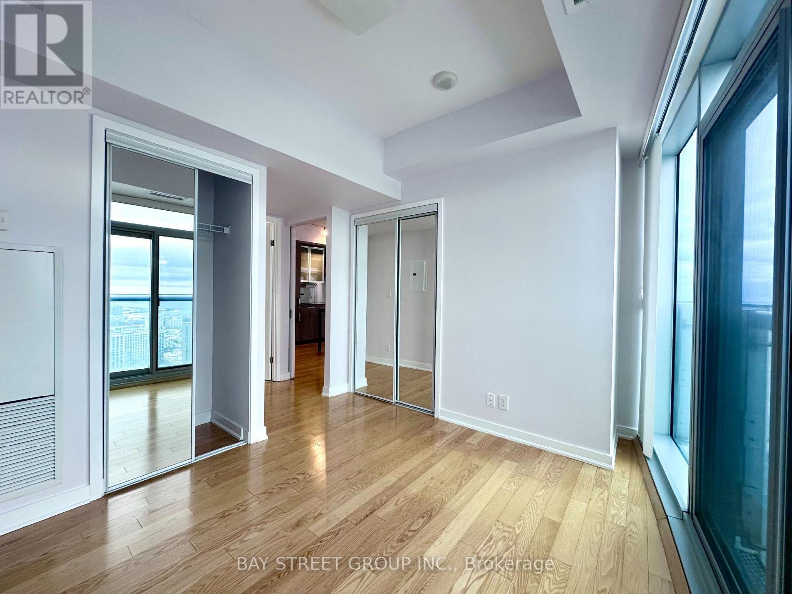 A spacious room with wooden floors and white walls, part of a Bay Street Group Inc. property.