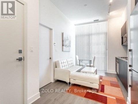 A white couch sits in a modern living room with a kitchen area in the background.