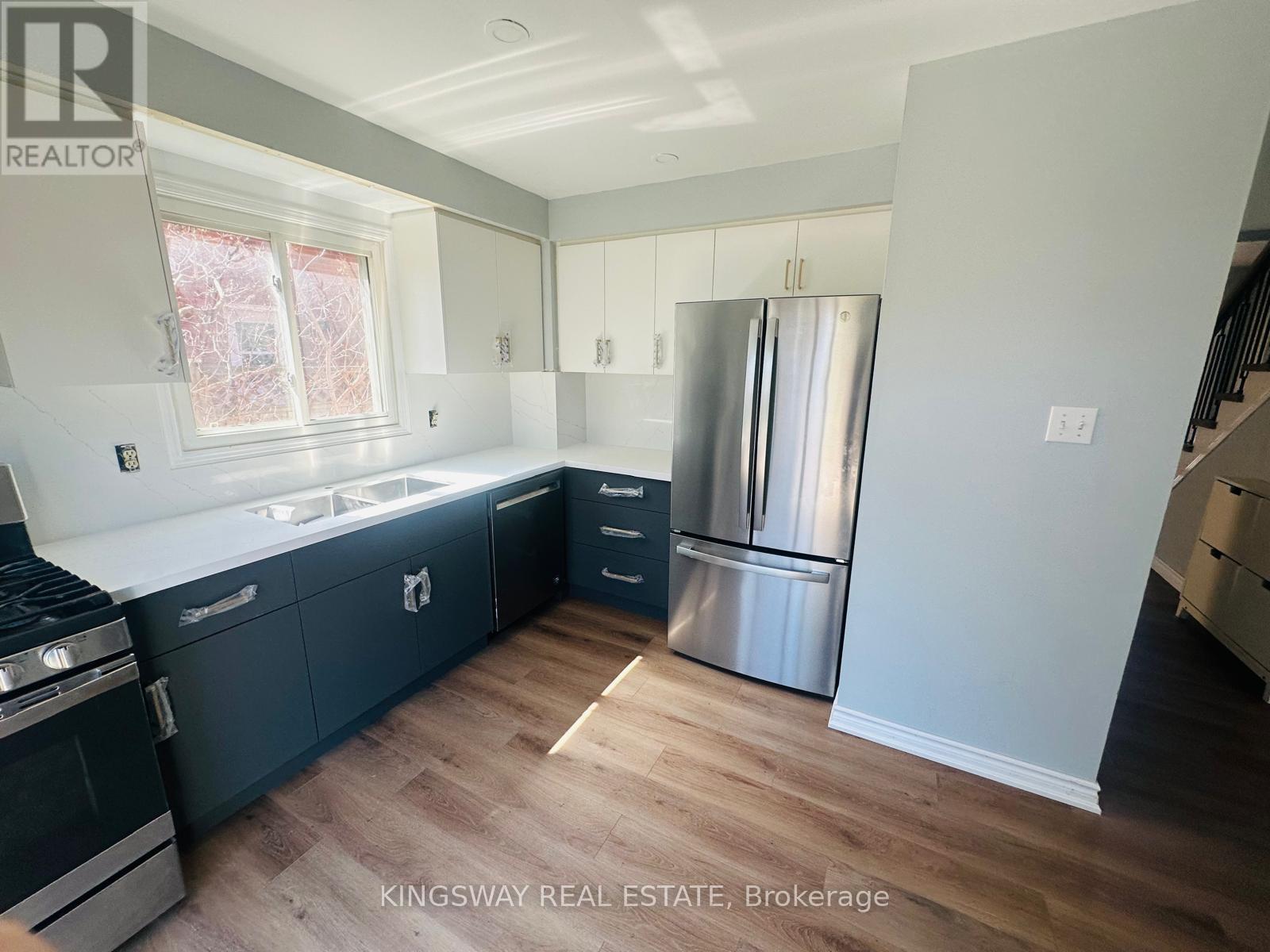 A kitchen with a stainless steel refrigerator and dark wood flooring.