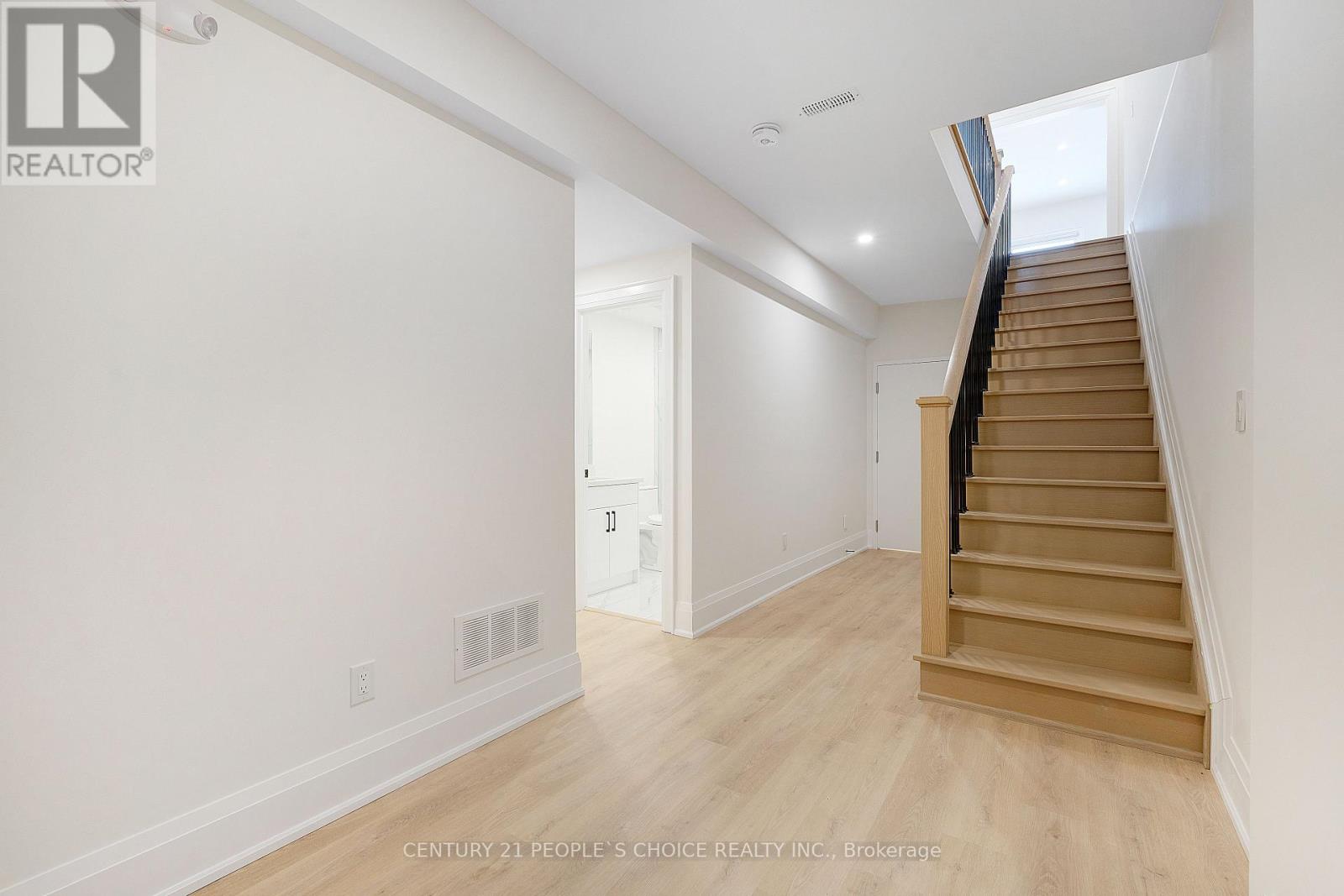 A spacious room with wooden floors and a staircase leading to another room.