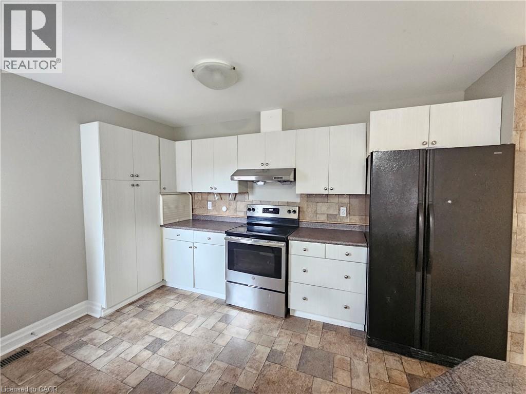A kitchen with a black refrigerator, white cabinets, and a tiled floor.