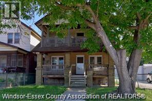 A tree in front of a house with a balcony.