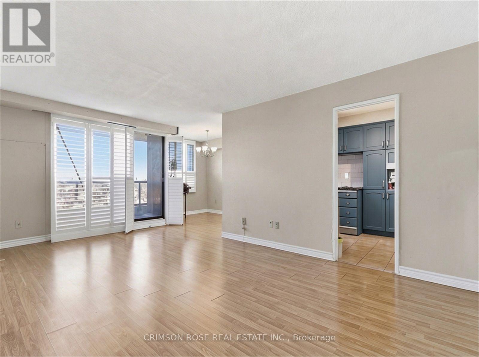 A spacious room with wooden flooring and a kitchen area in the background.