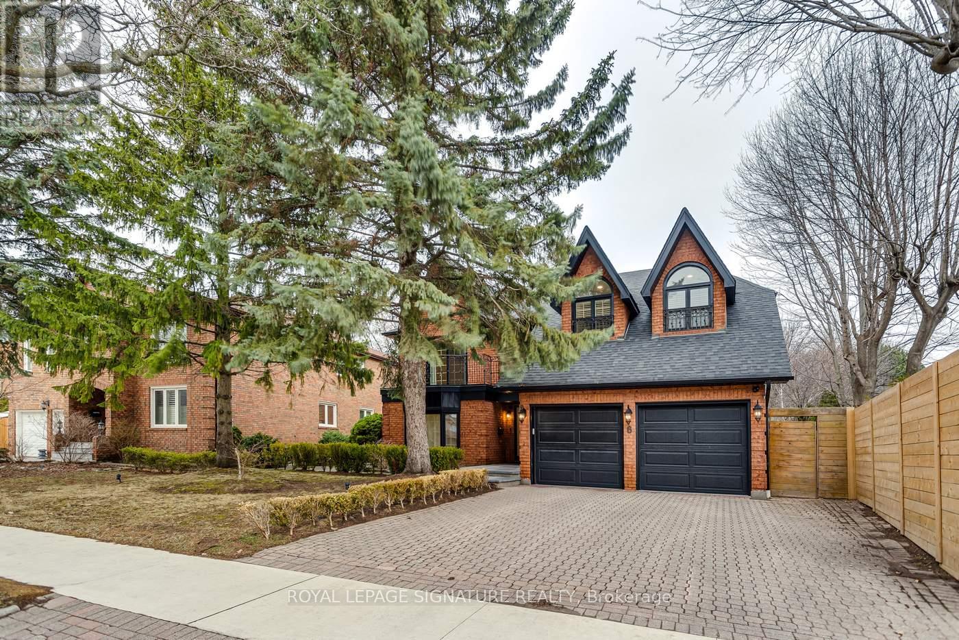 A house with a brick facade and a black garage door is surrounded by trees.