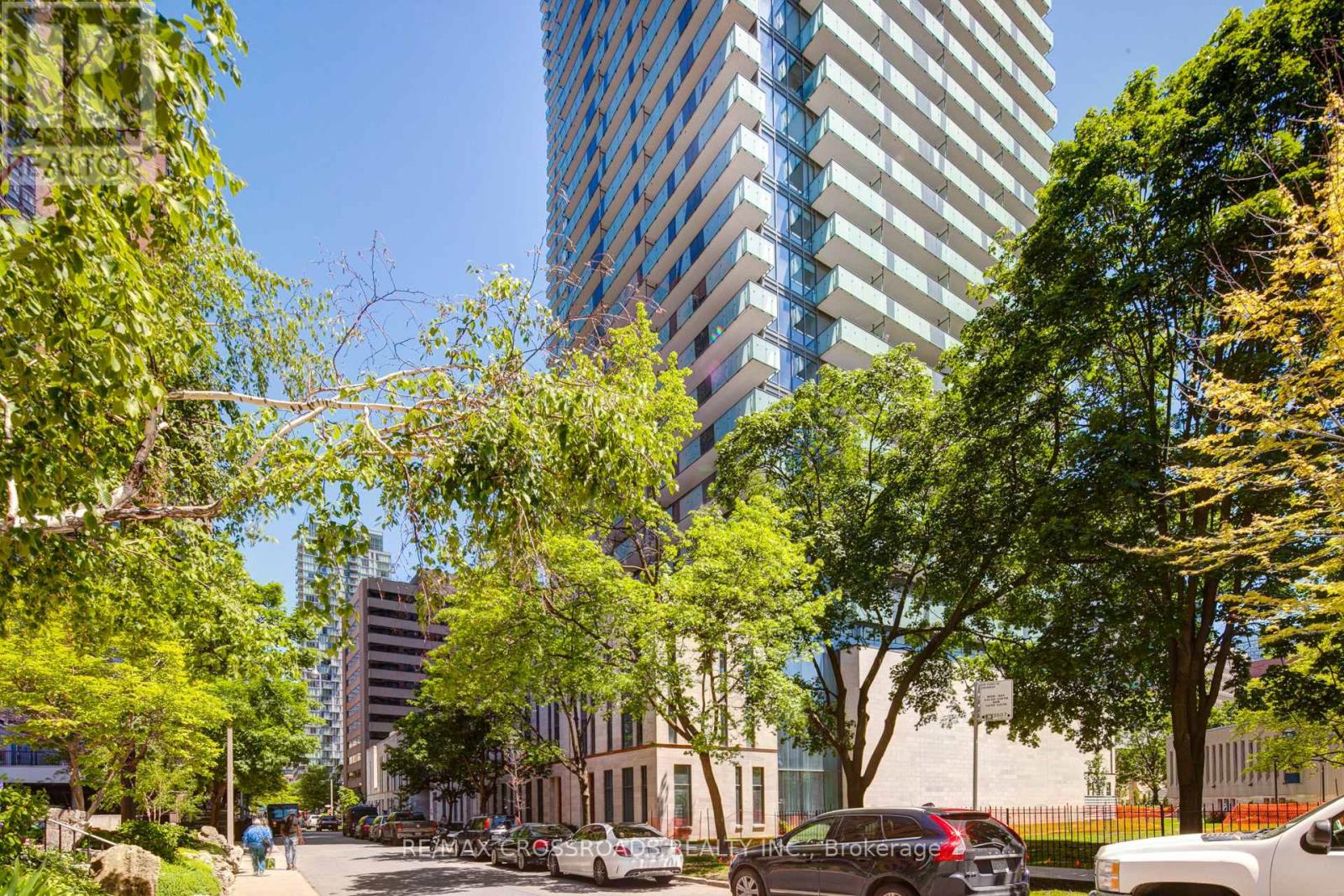 A city street with cars and trees in the foreground and a tall building in the background.