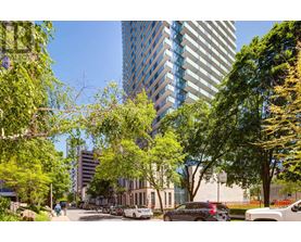 A city street with cars and trees in the foreground and a tall building in the background.