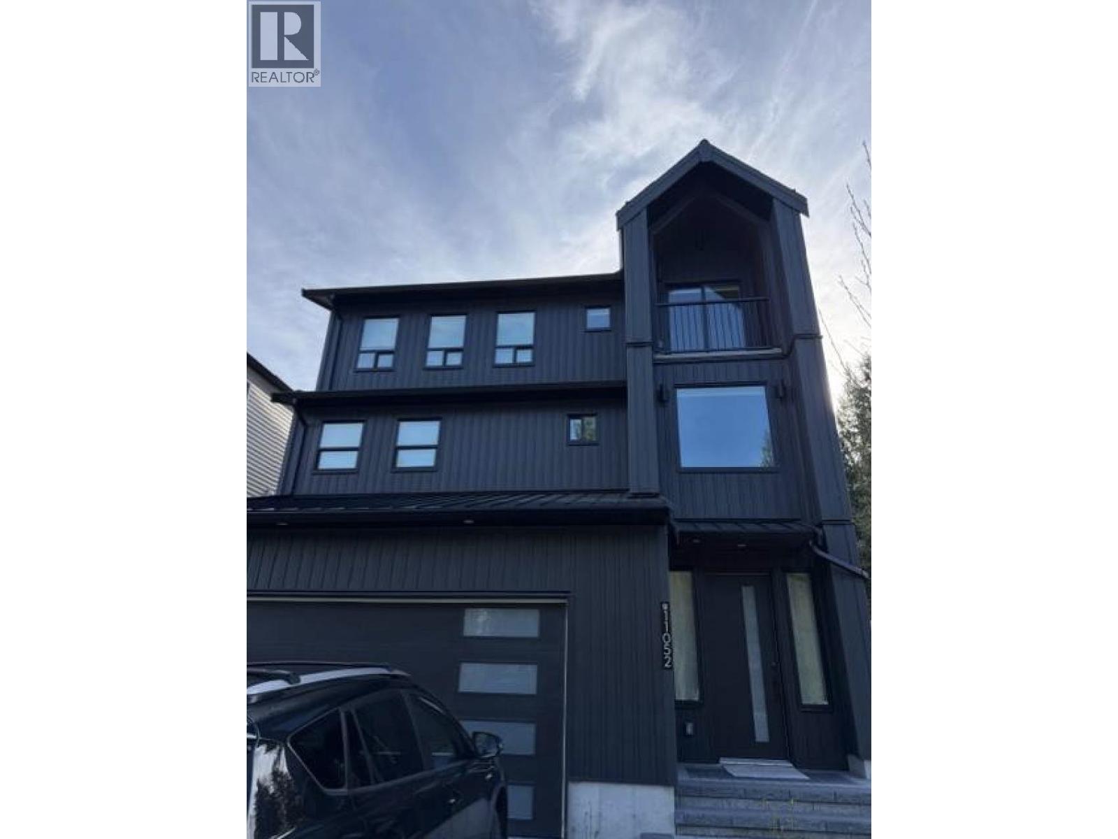 A modern house with a black exterior and a car parked in front.