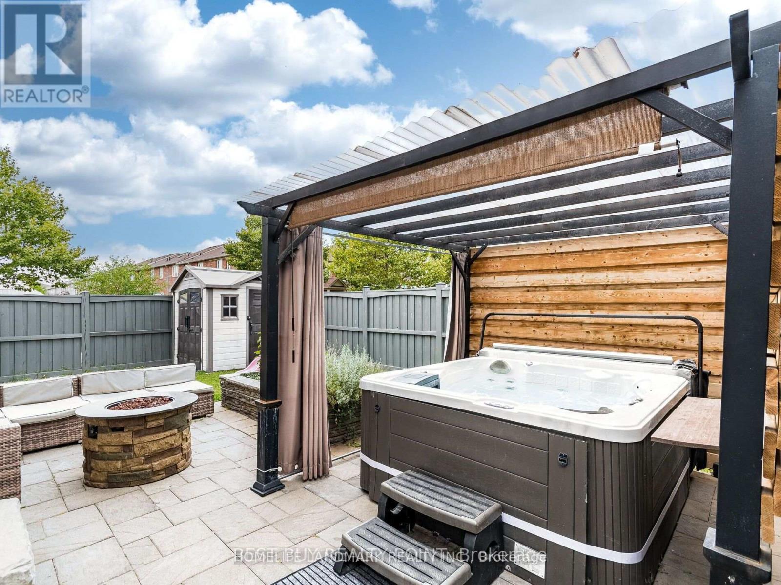 A hot tub is in the middle of a patio with a wooden pergola above it.
