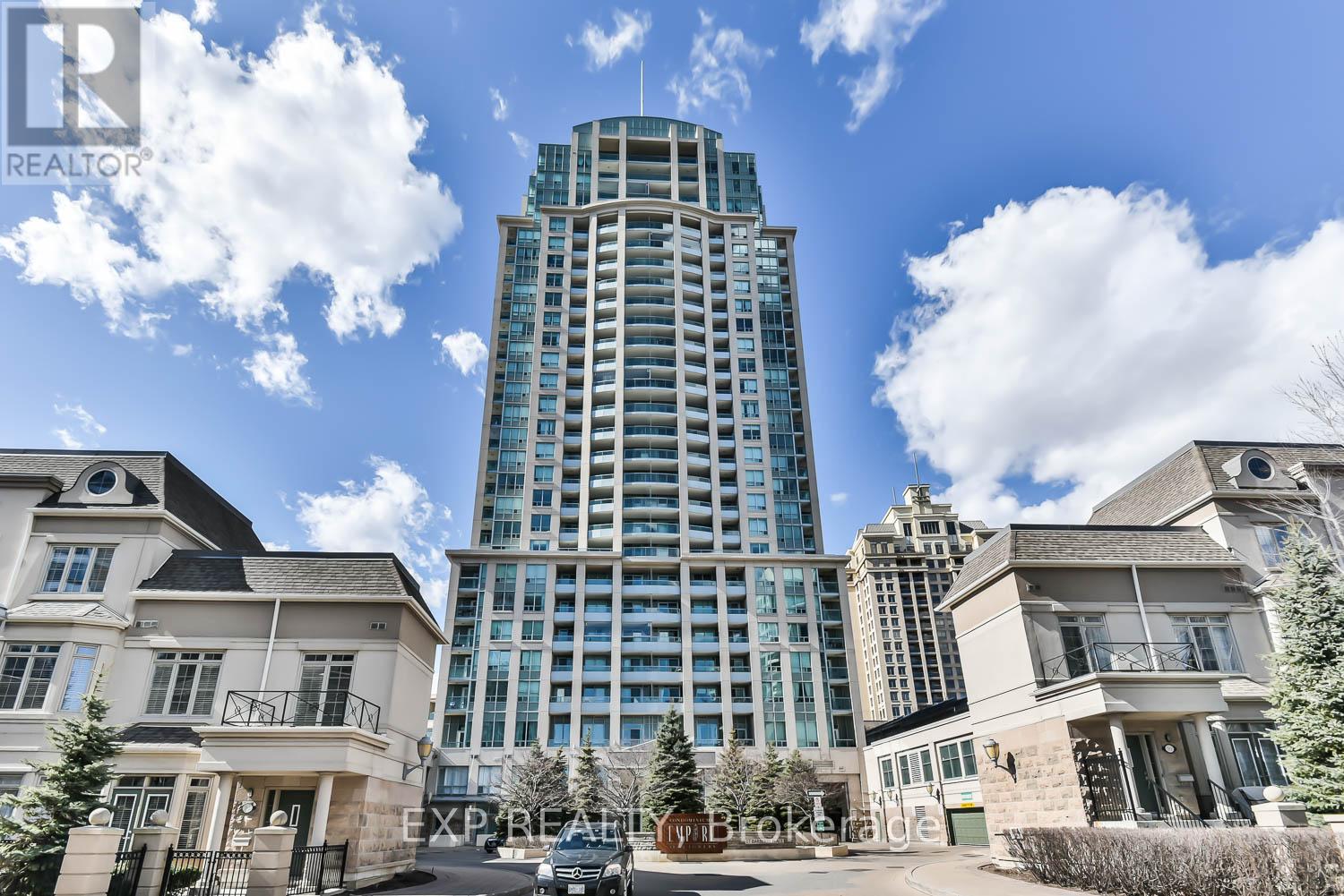 A tall building with a glass facade stands in front of two smaller houses.