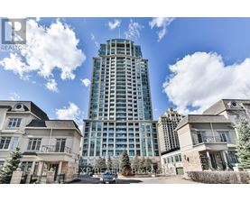 A tall building with a glass facade stands in front of two smaller houses.