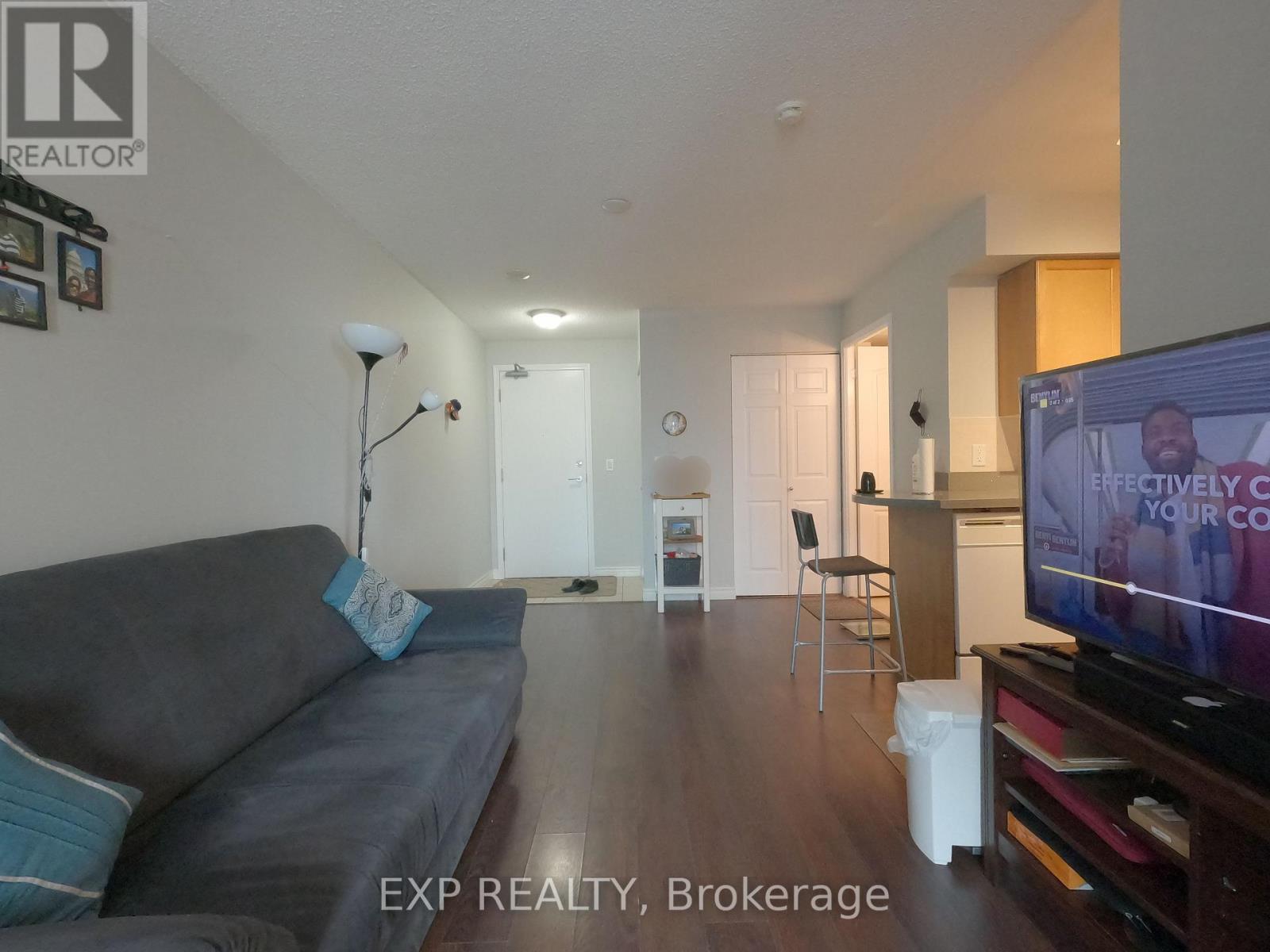 A living room with a grey couch and a television on.