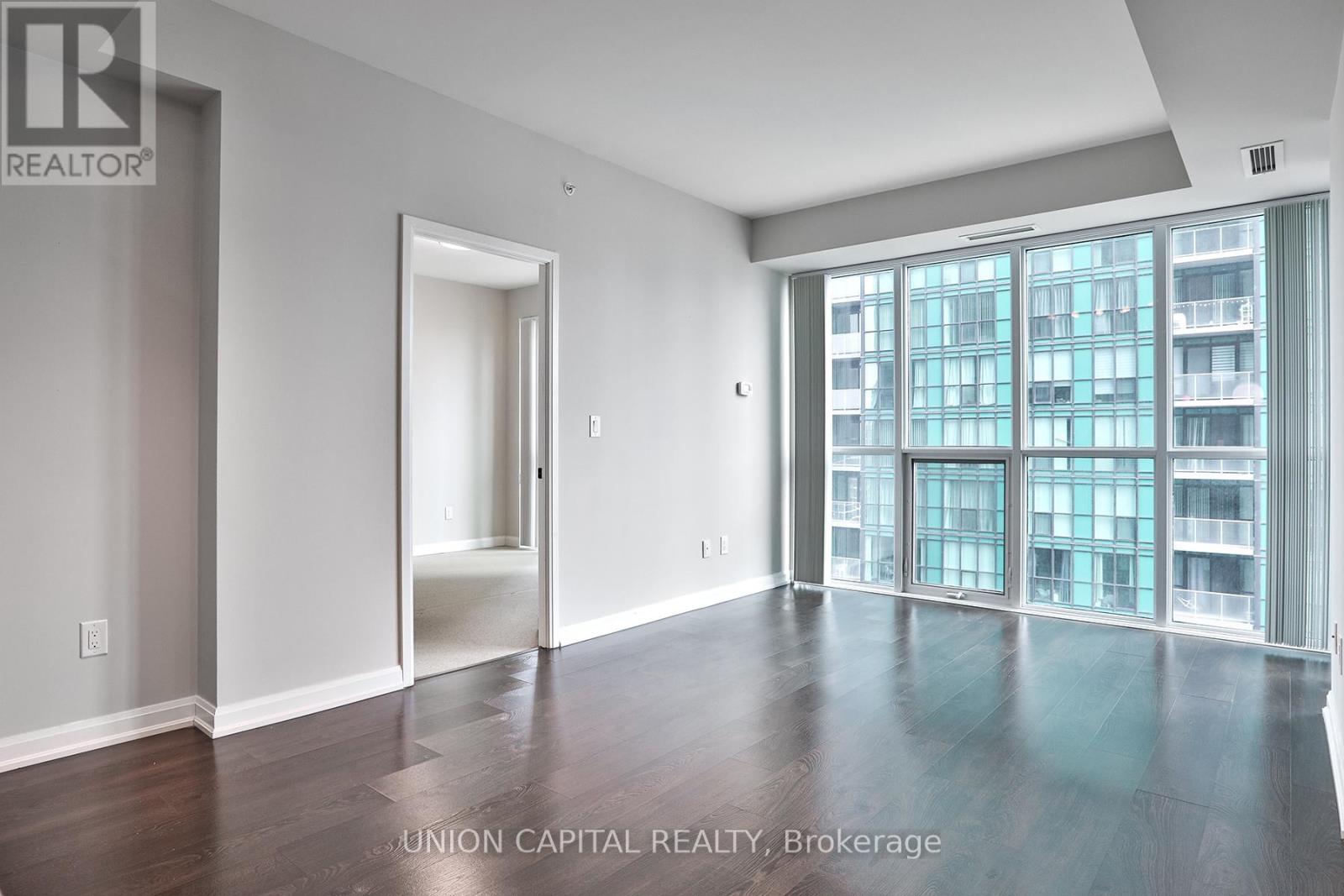 A spacious room with wooden floors and a large window overlooking a building.
