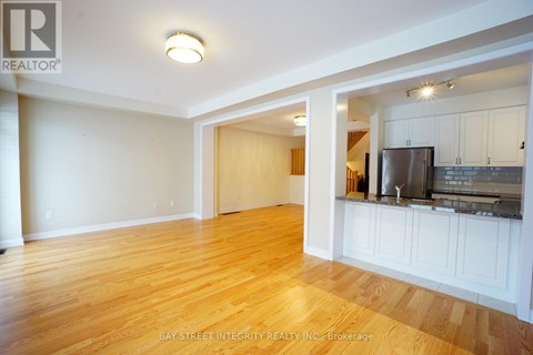A spacious room with wooden floors and white walls, featuring a kitchen area with a refrigerator, microwave, and cabinets.