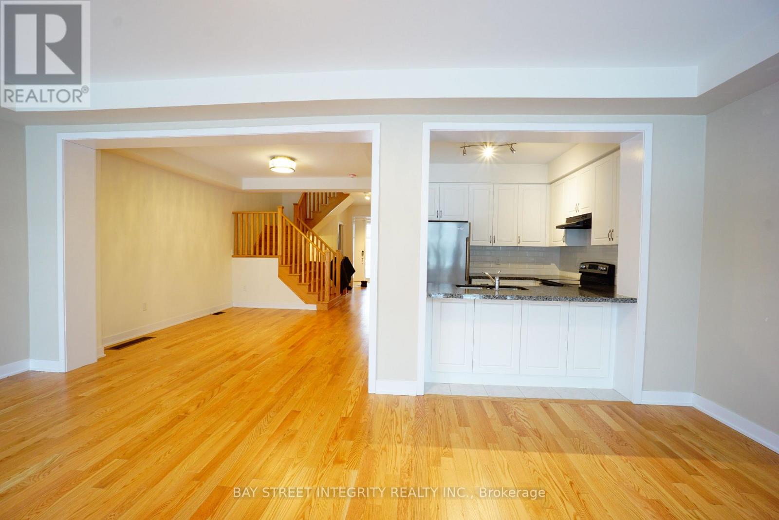 A spacious room with wooden floors and a kitchen area with white cabinets.
