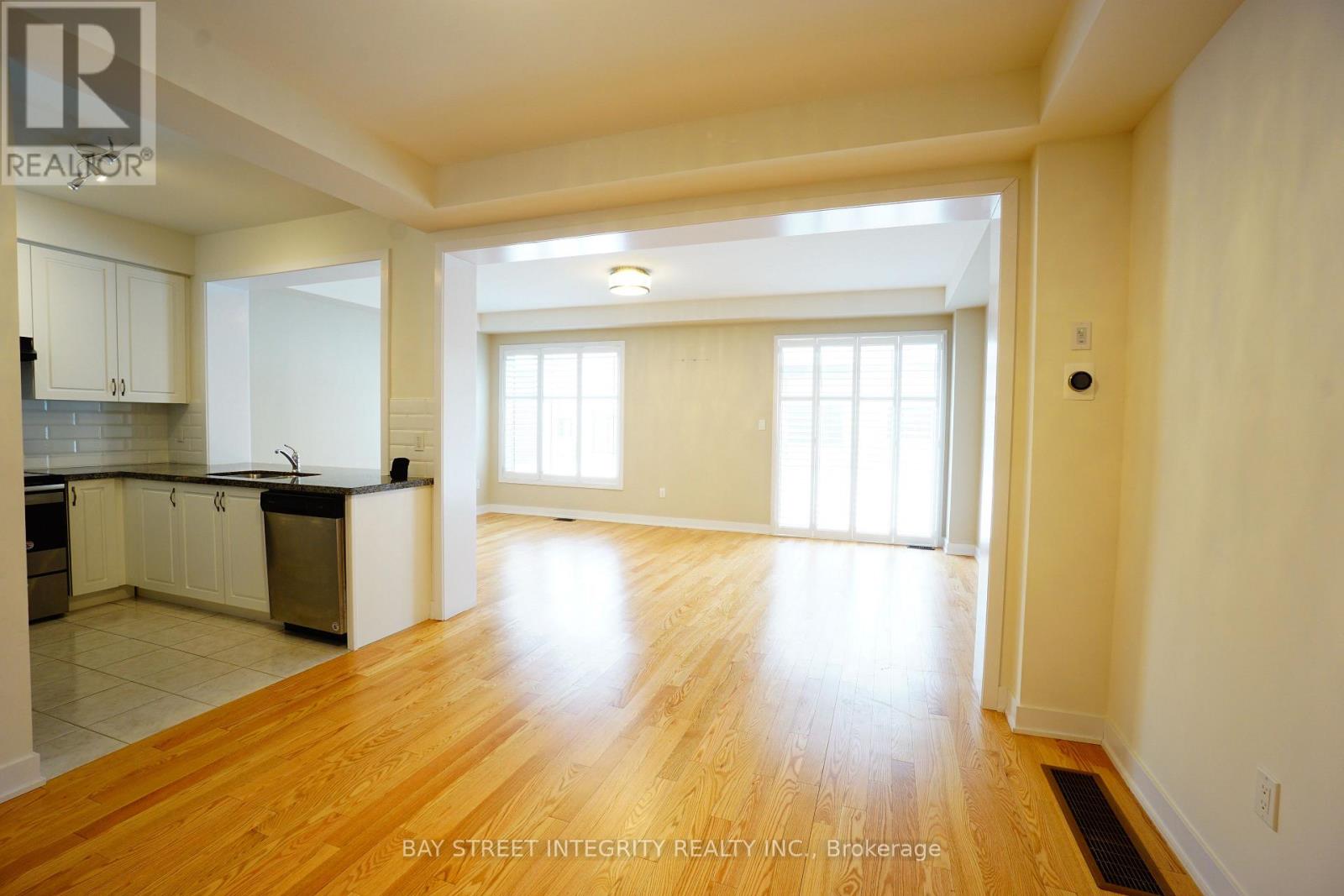 A spacious living room with wooden floors and a kitchen area in the background.