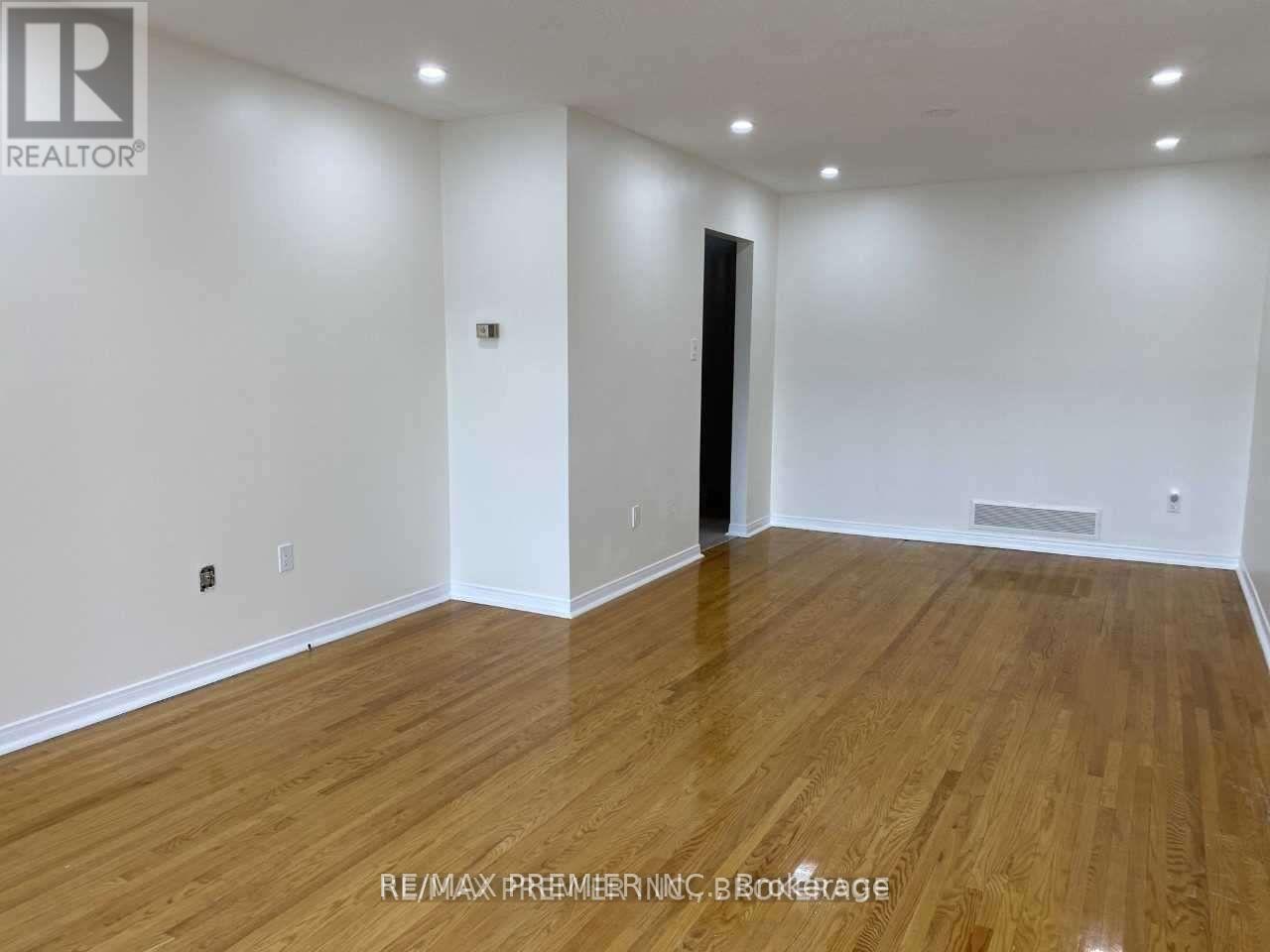 A room with wooden flooring and white walls, with a black door on the right.