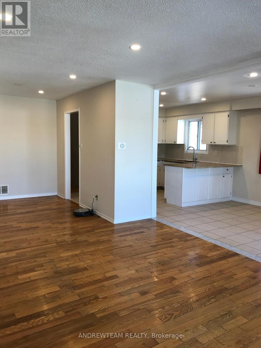 A room with wooden flooring and a kitchen area in the background.