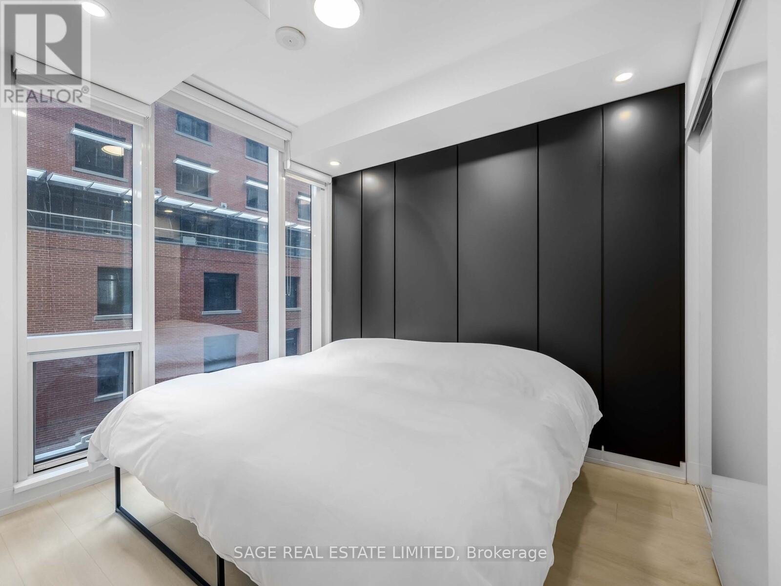 A bedroom with a large bed and a view of a brick building outside the window.