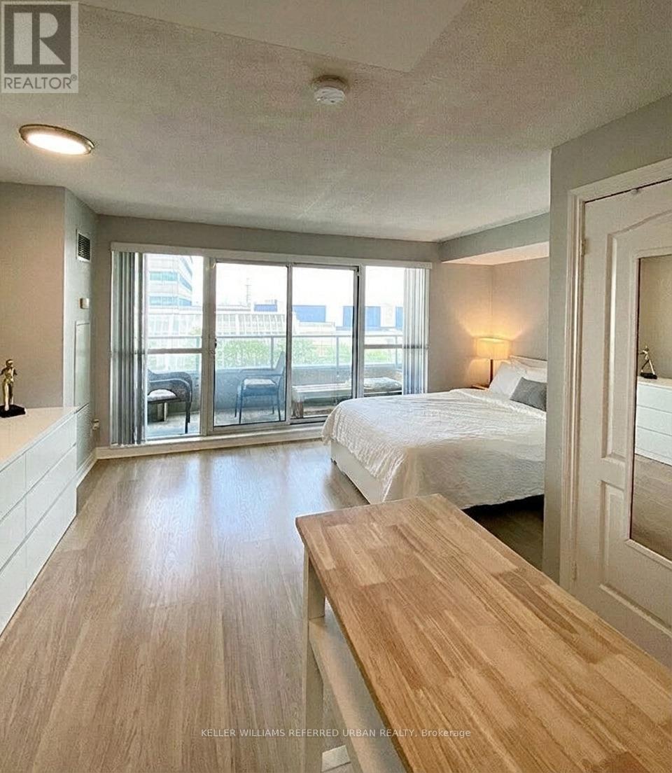 A bedroom with a bed, a bench, and a window with a view of the city.