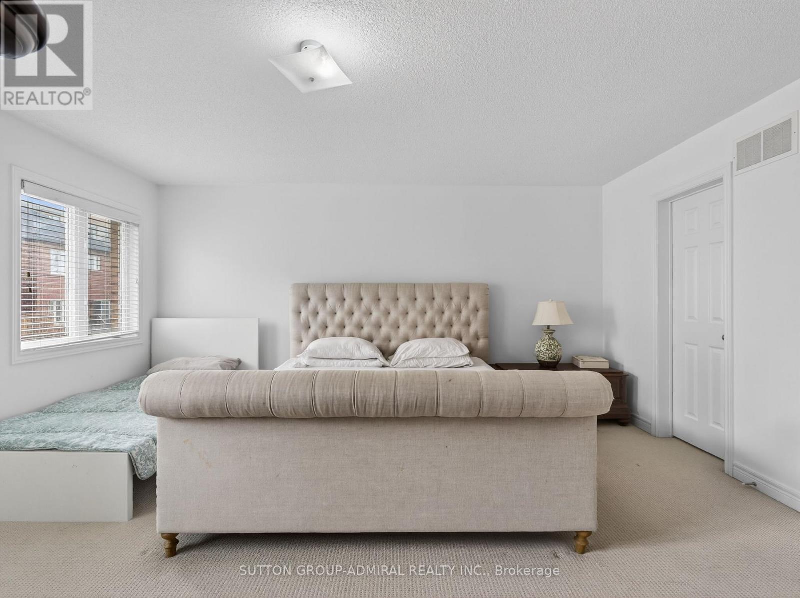 A bedroom with a large bed and a window with blinds.
