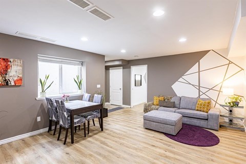 A modern living room with a grey sofa and a dining table with chairs.