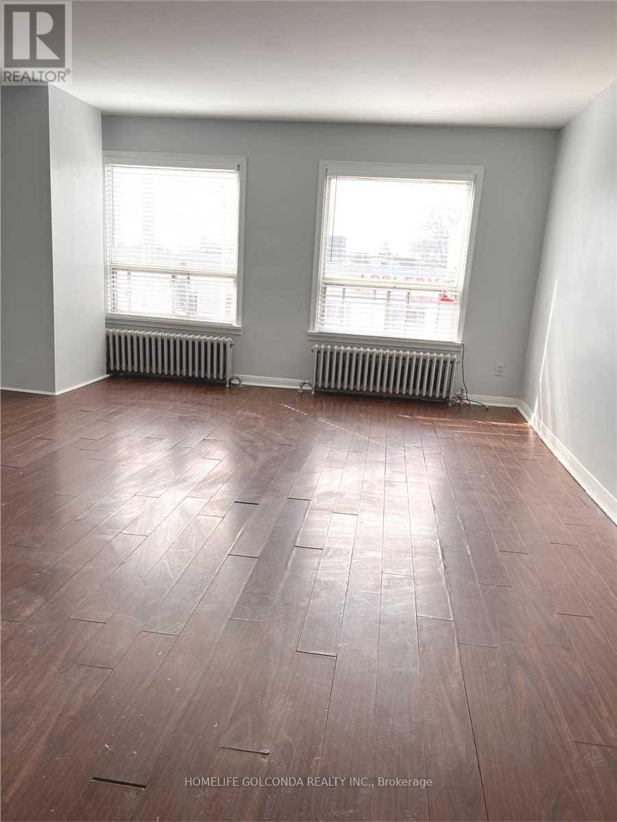 A room with wooden flooring and two windows.