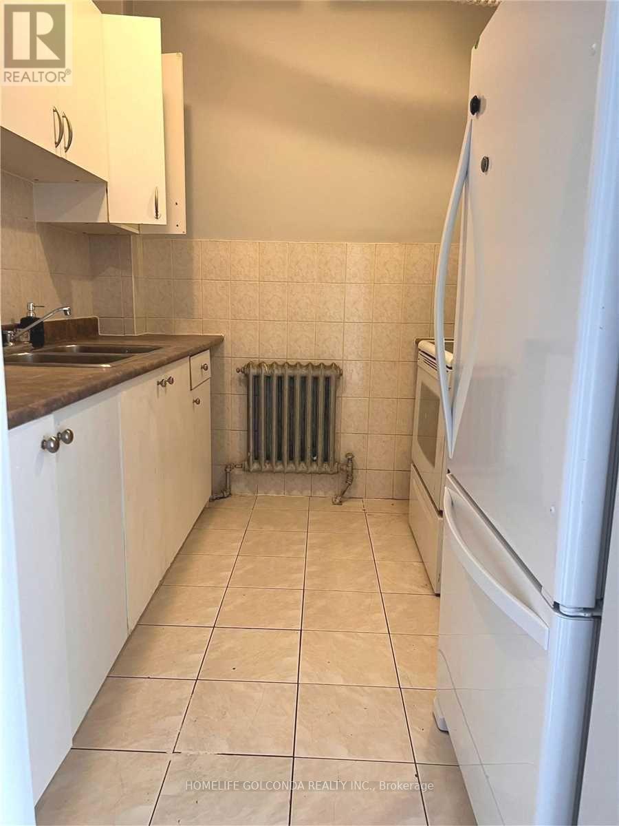 A white refrigerator stands in a kitchen with white cabinets and a white tile floor.