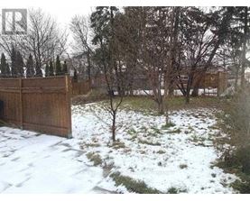 A snow-covered ground with a wooden fence and bare trees in the background.
