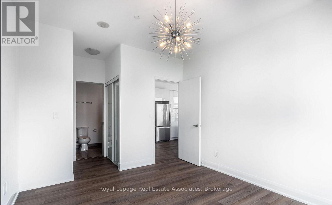 A spacious room with a wooden floor and white walls, featuring a large chandelier and a doorway leading to another room.