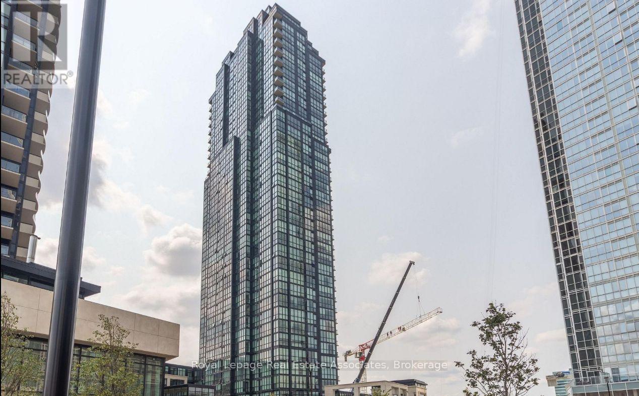 A tall glass building stands in front of a crane and other buildings.