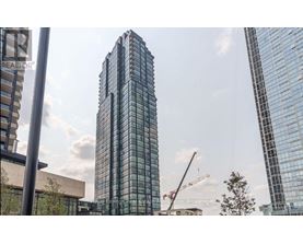 A tall glass building stands in front of a crane and other buildings.