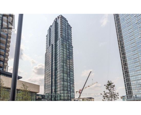 A tall glass building stands in front of a crane and other buildings.