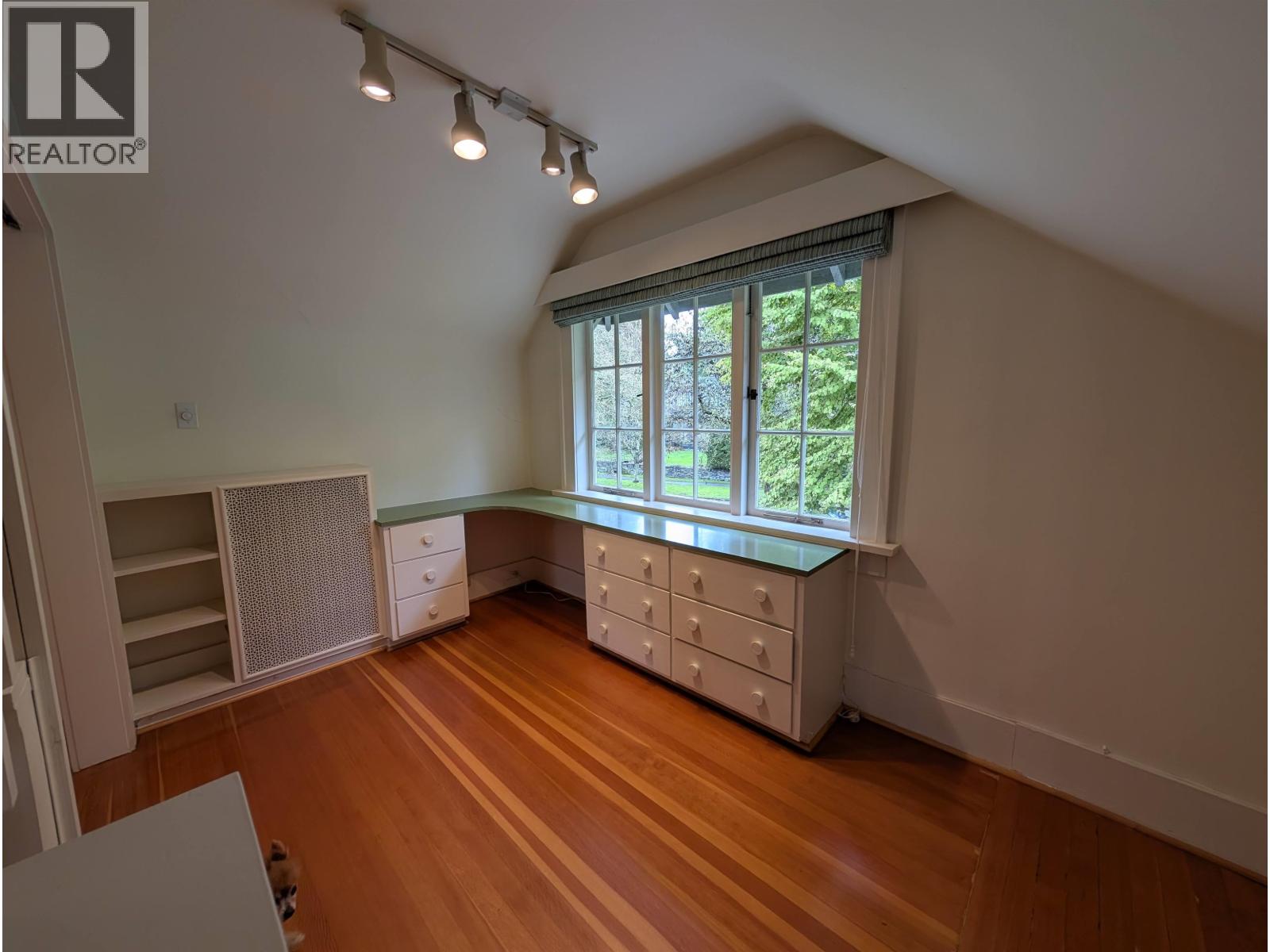 A room with wooden floors and a window with a view of trees.