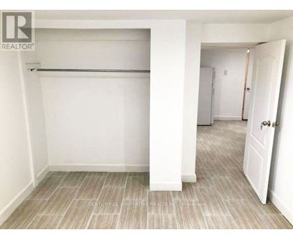 A white bedroom with a large bed and a doorway leading to another room.