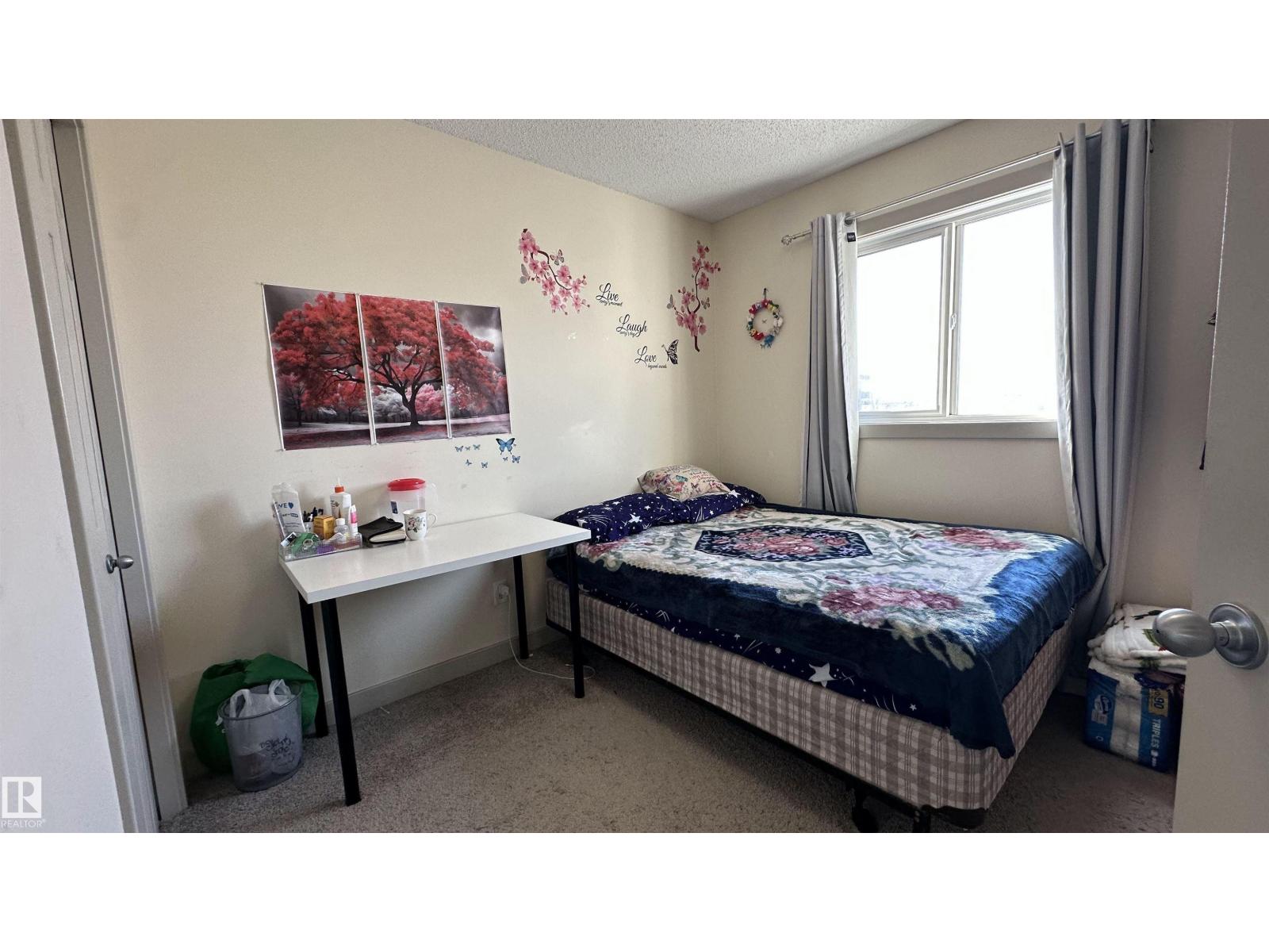 A bedroom with a bed, desk, and a wall decorated with flowers and a tree picture.