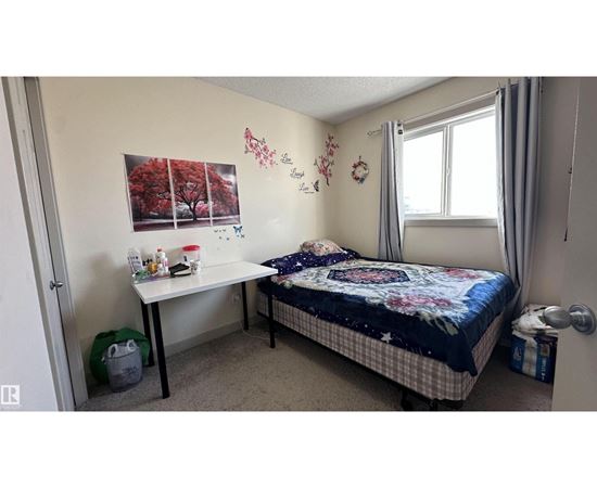 A bedroom with a bed, desk, and a wall decorated with flowers and a tree picture.