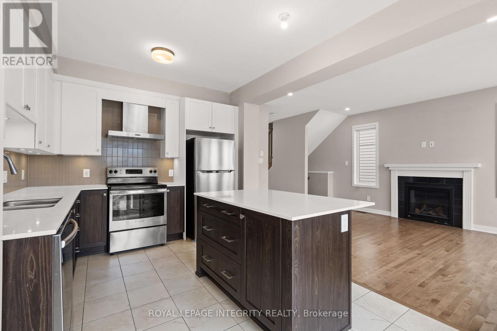 A modern kitchen with a stainless steel refrigerator, oven, and a fireplace in the living room.