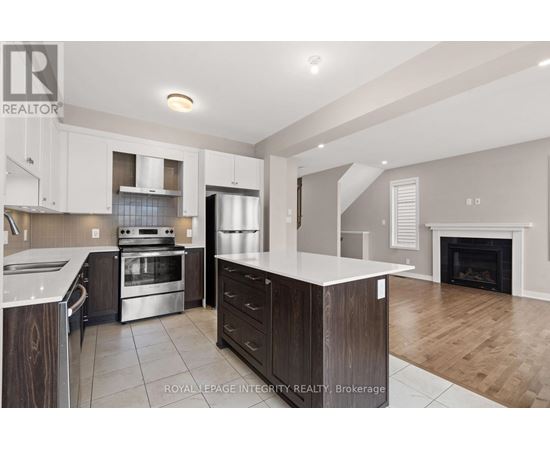 A modern kitchen with a stainless steel refrigerator, oven, and a fireplace in the living room.