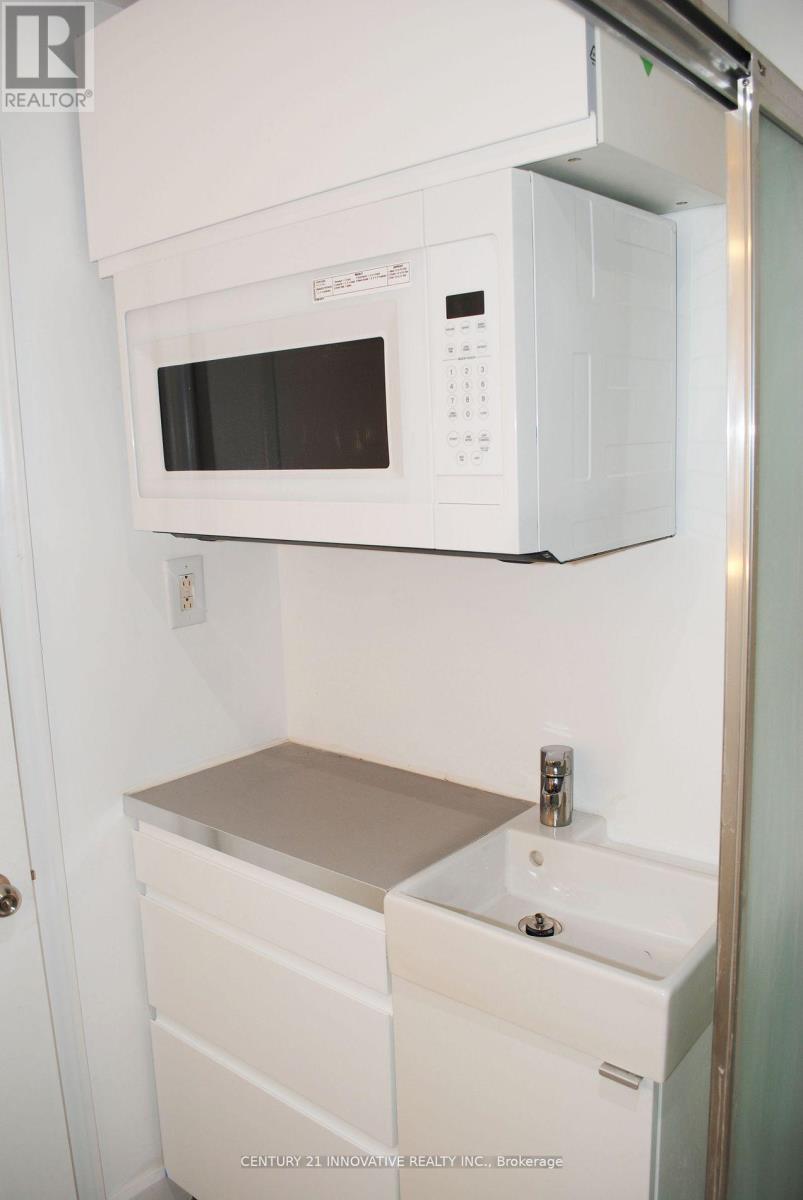 A white microwave oven is mounted above a white sink in a small kitchen.
