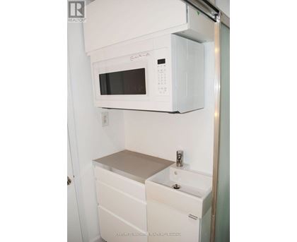 A white microwave oven is mounted above a white sink in a small kitchen.