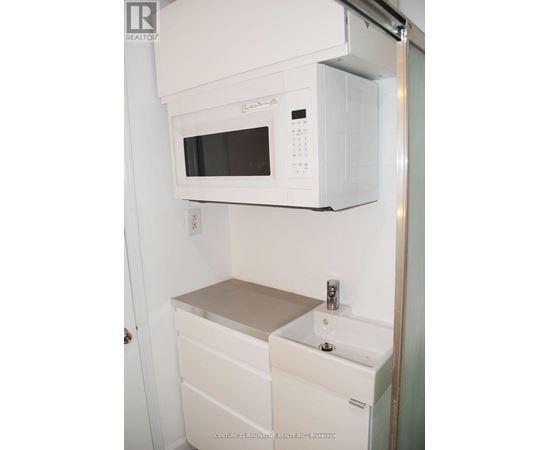 A white microwave oven is mounted above a white sink in a small kitchen.