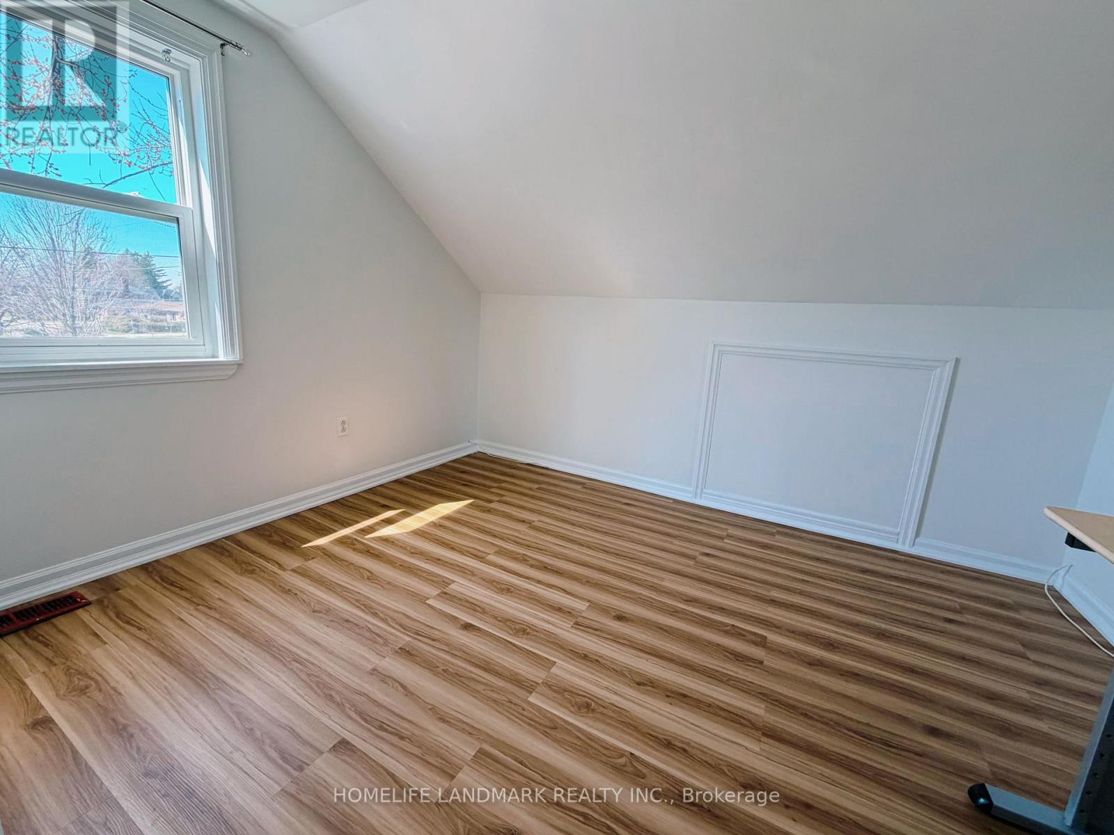 A room with wooden flooring and a window showing trees outside.