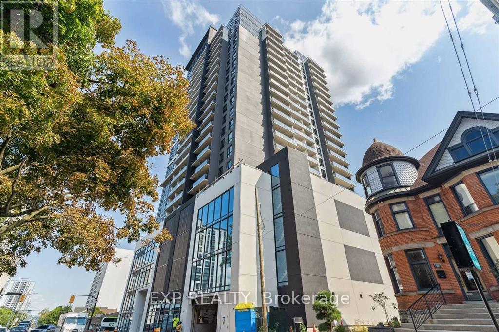 A modern building with a curved glass facade stands next to a tree with autumn leaves.