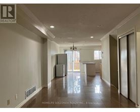 A spacious, empty room with a refrigerator and a table in the middle.