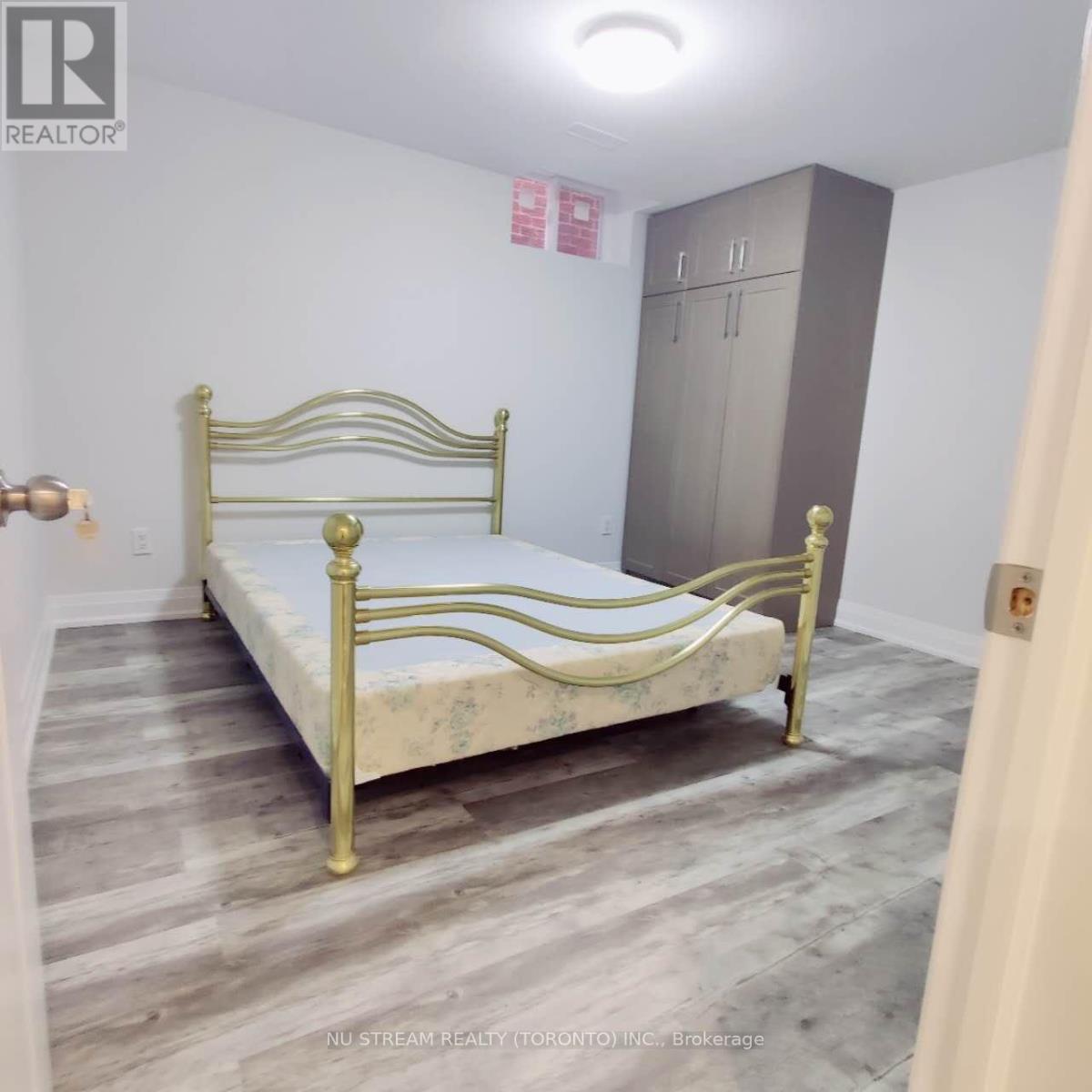 A bedroom with a bed, wardrobe and a brokerage sign.