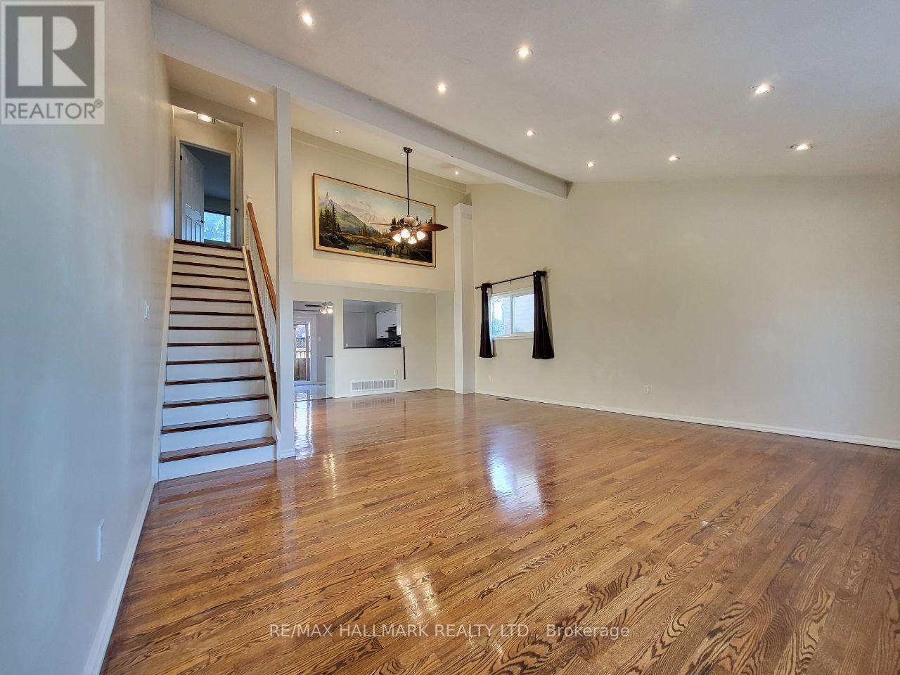 A spacious room with wooden flooring and a staircase leading to another level.