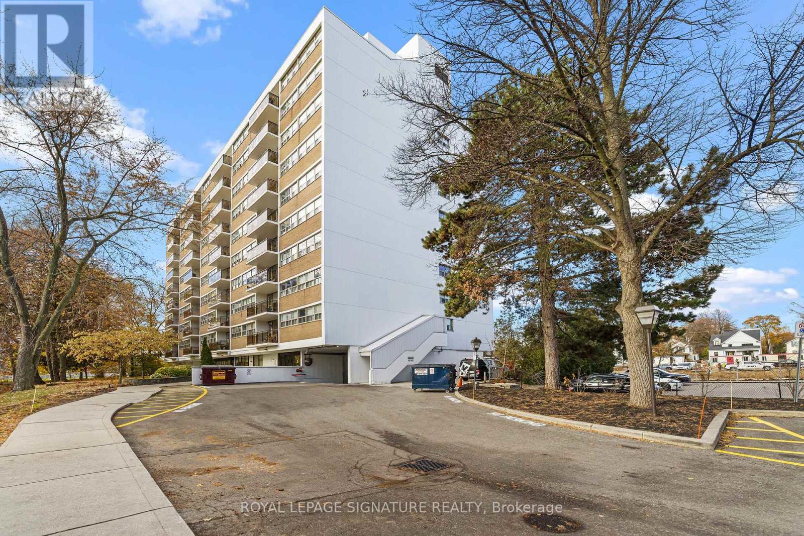 A tall building with a white facade is surrounded by trees and a parking lot.