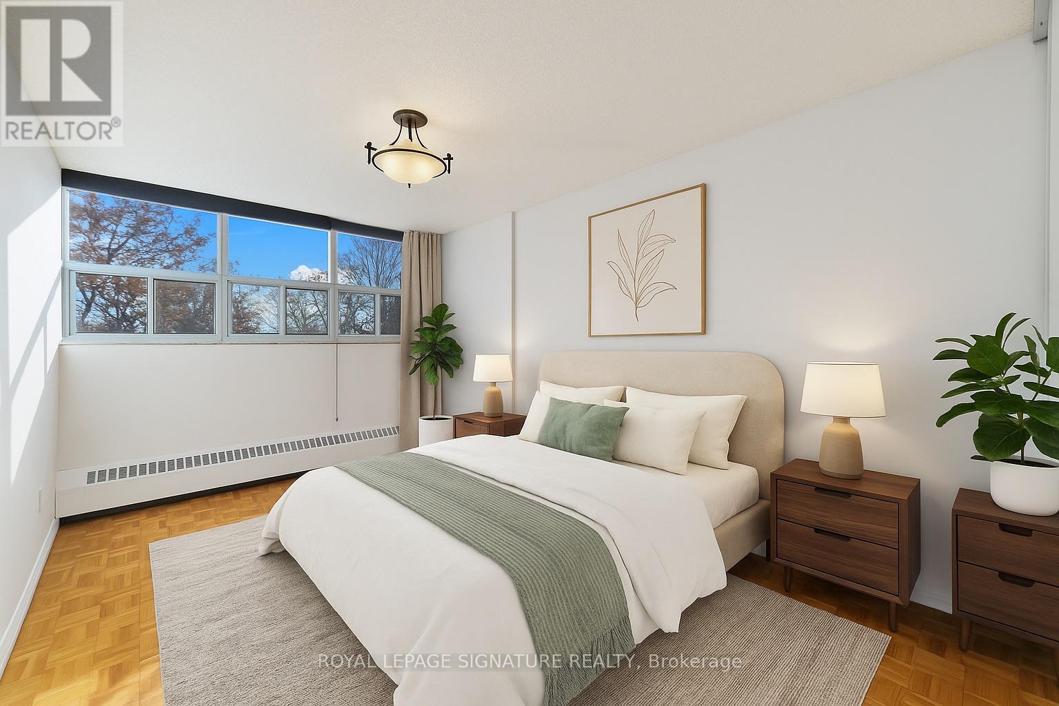 A bedroom with a large bed, a nightstand, and a window with a view of trees outside.