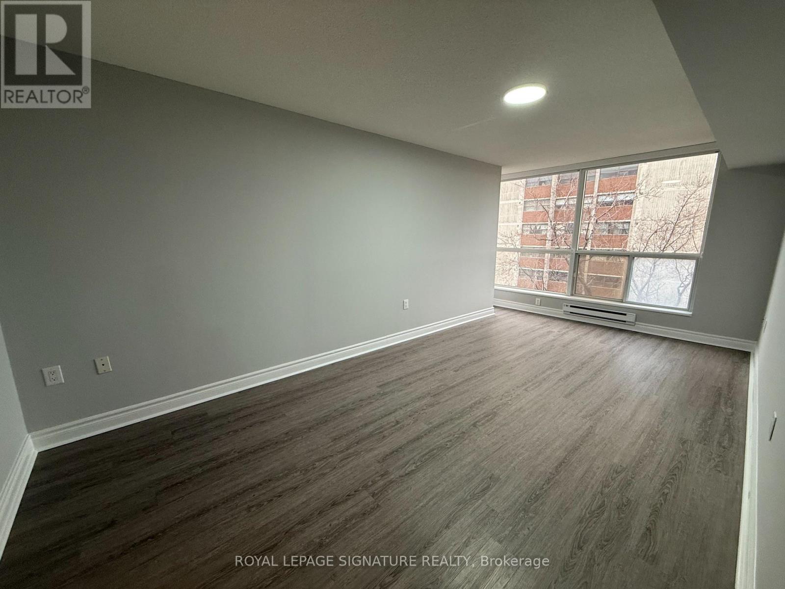 A room with wooden flooring and a window overlooking a building.