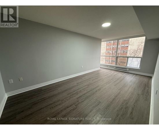 A room with wooden flooring and a window overlooking a building.